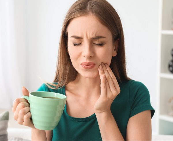 woman with coffee mug touching her cheek in pain