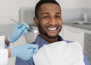 young adult man smiling in the dental chair as the dentist uses tools to examine his mouth