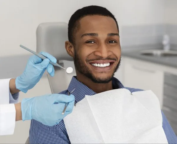 young adult man smiling in the dental chair as the dentist uses tools to examine his mouth
