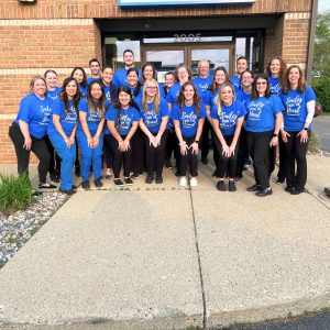 Contemporary Family Dental Team posing outside brick Grand Rapids Dental Office in Blue Smiles from the Heart T-Shirts